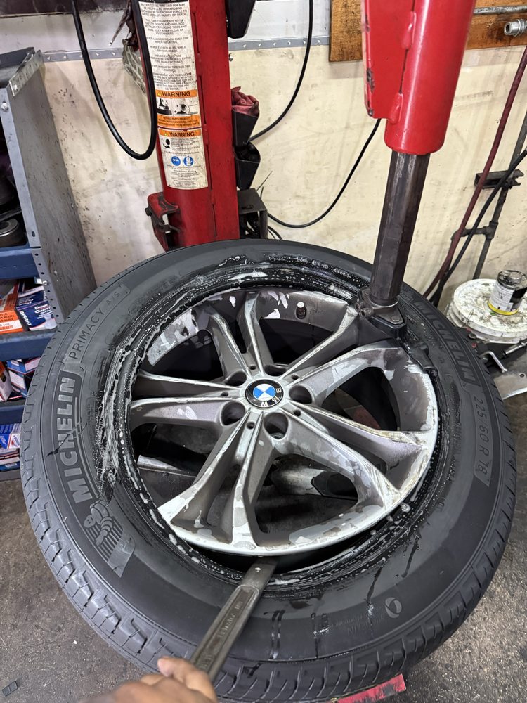A silver BMW wheel and tire leaning against a tire changing machine inside a service van or shop.