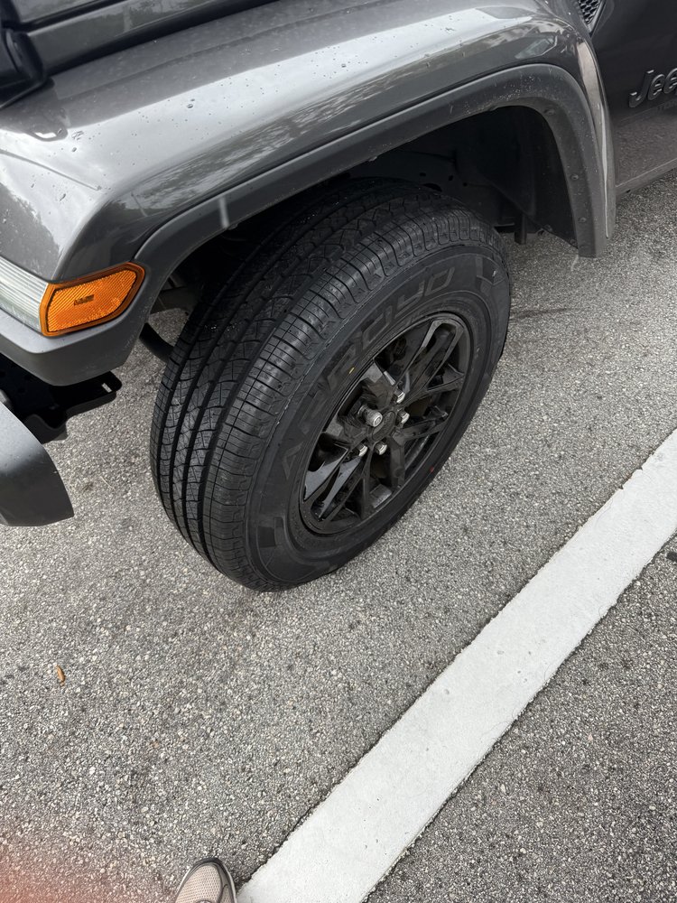 Front wheel and tire of a dark gray or black Jeep parked on asphalt.
