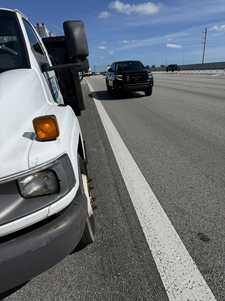 A white commercial van parked on the side of a highway as traffic passes by.