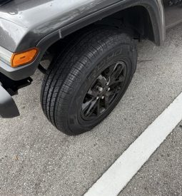 Front wheel and tire of a dark gray or black Jeep parked on asphalt.